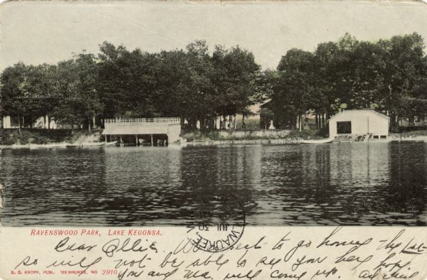 View across lake towards Ravenswood Park. Two boathouses are on the shoreline, and behind trees are cabins. Caption reads: "Ravenswood Park, Lake Kegonsa."