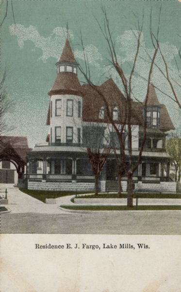 View from street towards a private home with a turret and front and side porch. There is a porte cochère in the driveway on the left. Caption reads: "Residence E.J. Fargo, Lake Mills, Wis."