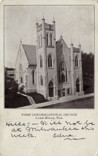 Elevated view across street towards the First Congregational Church. There are two front entrances, a bell tower and a large stained-glass window. Caption reads: "First Congregational Church, Lake Mills, Wis."