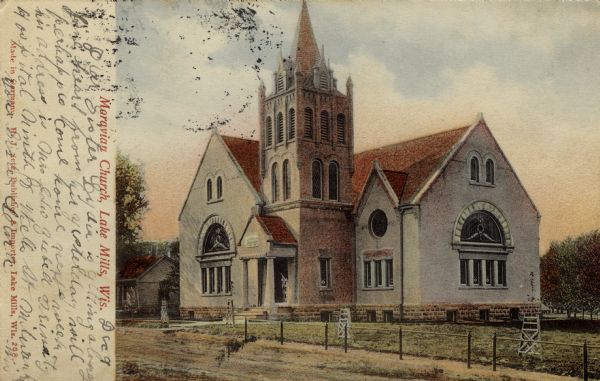 View across unpaved road towards a brick church with Romanesque arches. Columns are at the entrance. Caption reads: "Moravian Church, Lake Mills, Wis."