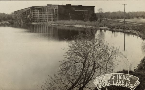 View of the Knickerbocker Ice Company building. Rock Lake in the foreground. There is a ramp leading from the lake to the ice house. Caption reads: "The Ice House, Rock Lake, Wis."
