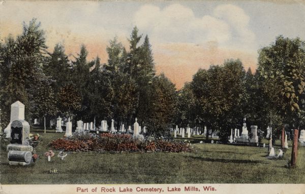 View of a cemetery with graves among trees. Place File: check Postcards, and add captions. Caption reads: "Part of Rock Lake Cemetery, Lake Mills, Wis."