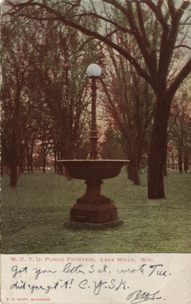 View of a fountain on a pedestal in a park. Caption reads: "W.C.T.U. Public Fountain, Lake Mills, Wis."