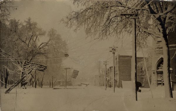 Photographic postcard view of a central street covered in snow and ice. There are downed power lines, with lines and trees coated with ice.
