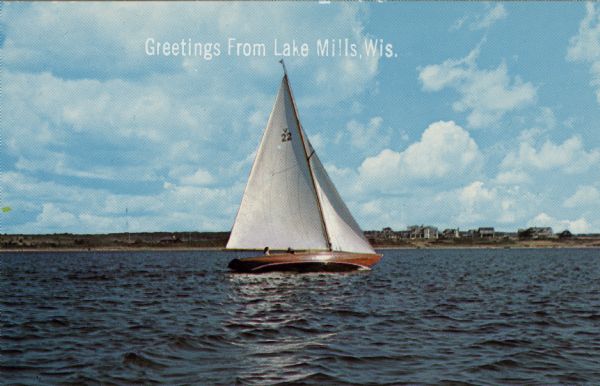View across water towards a single-masted sailboat with two passengers sailing in Rock Lake. Dwellings are along the far shoreline. Caption reads: "Greetings from Lake Mills, Wis."