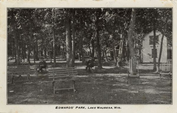 View of a park. Men in suits are sitting on the benches. Cottages are behind the trees. Caption reads: "Edwards' Park, Lake Waubesa, Wis."