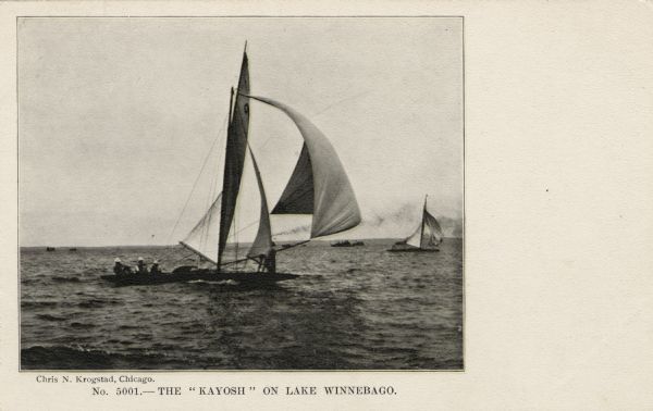 View across water towards a three masted sailboat with a crew of four men in Lake Winnebago. More boats are in the background.