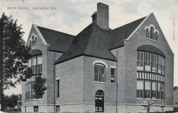 View towards the corner of a brick school building with distinctive arched windows on both sides. Caption reads: "North School, Lancaster, Wis."