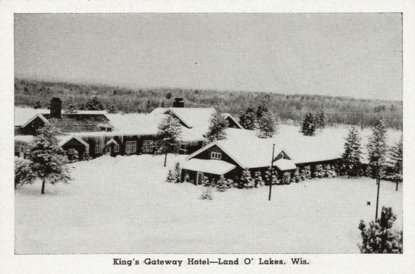 Elevated view of a hotel with multiple buildings. Heavy snow is on the ground and on the trees, and icicles are along the roofs of the buildings. Caption reads: "King's Gateway Hotel — Land O' Lakes, Wis."