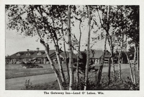 View through birch trees and across a road towards a hotel. Caption reads: "The Gateway Inn — Land O' Lakes, Wis."