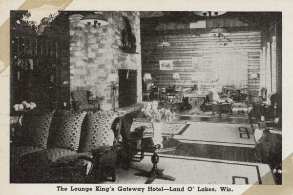 Interior view of a hotel lounge with a large fireplace, sofas and chairs. Caption reads: "The Lounge King's Gateway Hotel, — Land O' Lakes, Wis."