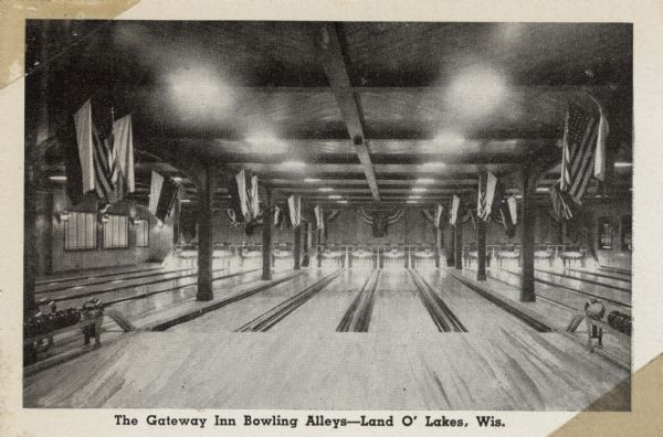 Interior view of the bowling lanes. Flags are hanging from the ceiling and along the back wall. Caption reads: The Gateway Inn Bowling Alleys — Land O' Lakes, Wis."