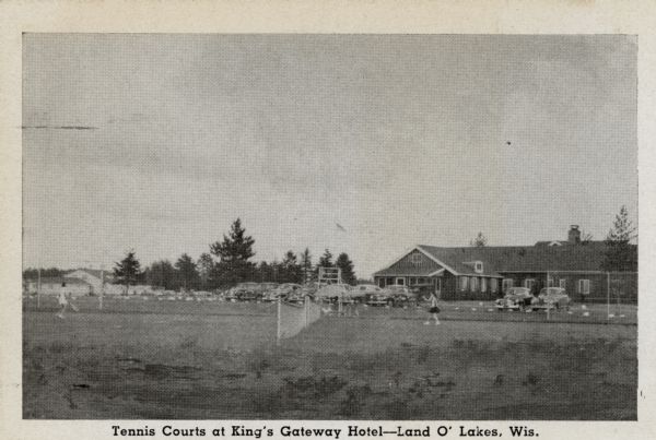 View of women playing tennis on a lawn court next to a parking lot. Caption reads: "Tennis Courts at King's Gateway Hotel — Land O' Lakes, Wis."