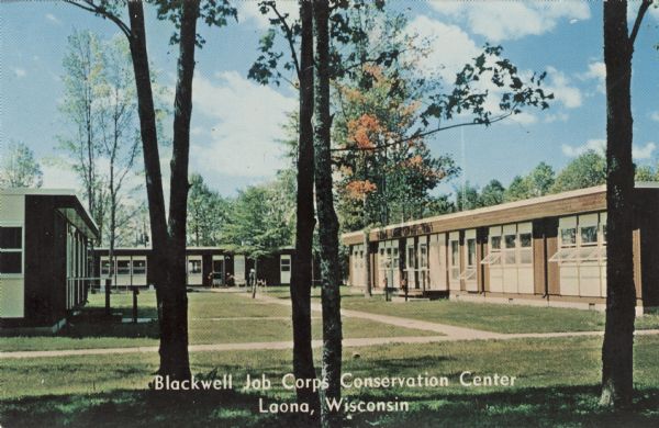 View of the buildings comprising the job center. Caption reads: "Blackwell Job Corps Conservation Center, Laona, Wis." Text on reverse reads: "Right — Pine Spruce Lodge, Left — Administration Building, Rear Center — Dining Room."