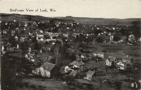 Elevated view of most of the town of Lodi, including churches, dwellings, businesses. Rolling hills on the horizon. Caption reads: "Bird's-eye [sic] View of Lodi, Wis."