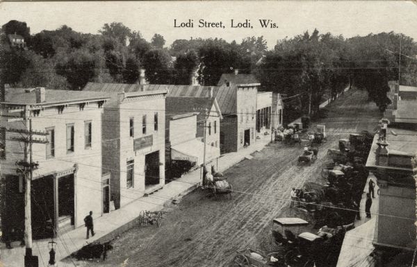 Elevated view of Lodi street in the central business district. There are horse-drawn vehicles, and pedestrians are on the sidewalks. Caption reads: "Lodi Street, Lodi, Wis."