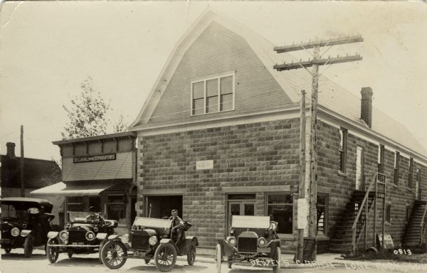 View of an auto service garage with Model T's parked in front. A storefront on the left has a sign for "De Laval Cream Separators" above the awning. Caption reads: "Dewey's Garage, Lone Rock, Wis."