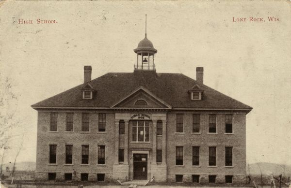 View towards the front of a brick two-story school building built in 1902. There is a bell tower on top of the roof. "Caption reads: "High School. Lone Rock, Wis."