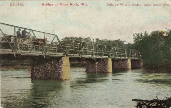 View across river towards a steel bridge with stone pylons on the Wisconsin River at Lone Rock. A horse-drawn wagon with two men is crossing over to the other side. Caption reads: "Bridge at Lone Rock, Wis."