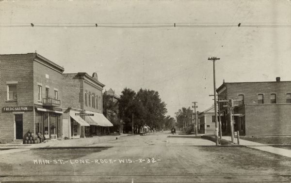 View of a small town main street at a railroad crossing. A restaurant is on the left, and a lunchroom is on the right. Caption reads: "Main St. — Lone Rock — Wis."