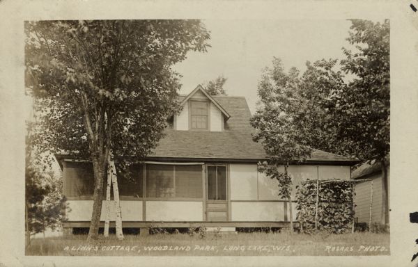 View across lawn towards a cottage with a screened-in porch, and birch trees in front. Caption reads: "A. Linn's Cottage, Woodland Park, Long Lake, Wis."