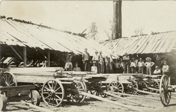 A group of men standing among a row of lumber wagons.