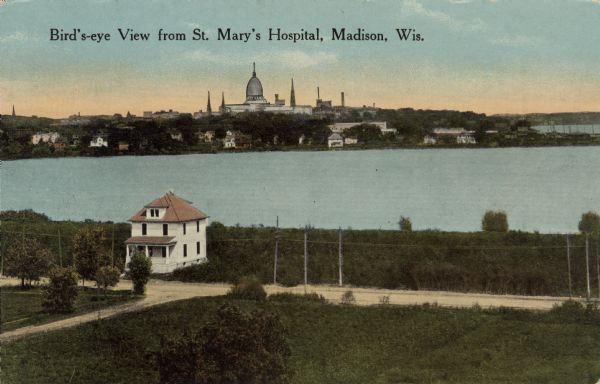 Colorized view across Monona Bay towards the Capitol. In the foreground is a field, trees, and unpaved roads with a single dwelling near the shoreline. Caption reads: "Bird's-eye View from St. Mary's Hospital, Madison, Wis."