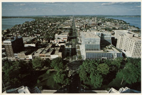 Elevated view of East Washington Avenue from the Wisconsin State Capitol. There is a glass bank building on the right side of East Washington Avenue. The YWCA building is on the far left. In the background Lake Mendota is on the left, and Lake Monona is on the right.