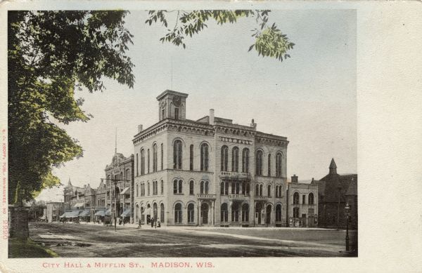 View across street towards City Hall located at 2 West Mifflin (corner with Wisconsin Avenue). The building has three stories and a clock tower. Caption Reads: City Hall & Mifflin St., Madison, Wis."