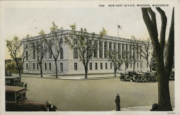 View across street towards the Post Office located at Monona Avenue (currently Martin Luther King Jr. Boulevard) and Doty Street. Automobiles are parked at the curbs and in the median. Caption Reads: "New Post Office, Madison, Wisconsin."