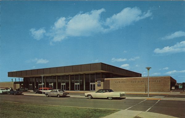 Exterior view of the main terminal of the Madison Airport. Automobiles are parked along the curb.