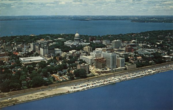 Color aerial postcard of the Isthmus from over Lake Monona. John Nolen Drive is along the shoreline in the foreground. The Wisconsin State Capitol is in the center.