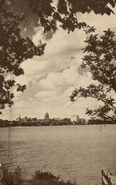 Sepia-toned postcard towards the Wisconsin State Capitol from across Lake Monona. There are trees and a pier in the foreground.