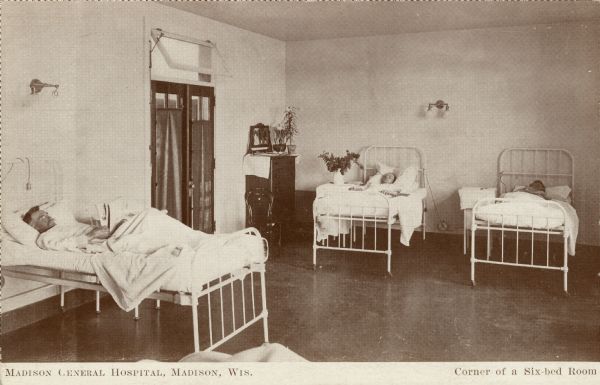 Interior view of a hospital room with patients in the beds. One patient is reading a newspaper. Caption reads: "Madison General Hospital, Madison, Wis.  Corner of a Six-Bed Room."