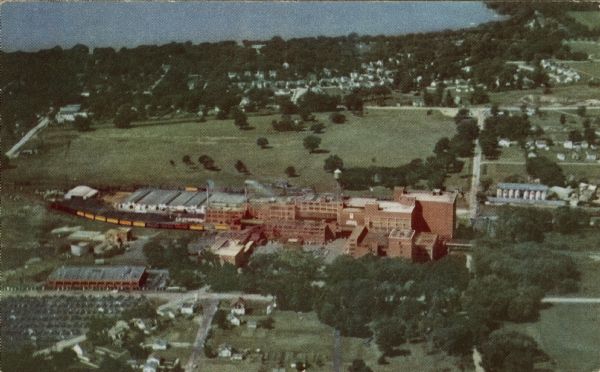 Aerial view of the Oscar Mayer & Co. with Lake Mendota in the distance. Text on reverse reads: "Pictured here in aerial color view is the meat packing plant of OSCAR MAYER & CO., at Madison. This plant is one of the nation's most modern and efficient, providing one of the best livestock markets in the middlewest. Readily accessible by railroad and highway, the plant enjoys a beautiful setting amid the sparkling lakes of Madison and the fertile farm lands of Southern Wisconsin."