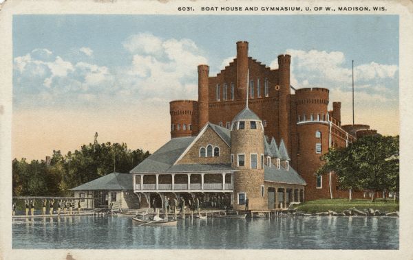 View of the boathouse and Red Gym from Lake Mendota. Men are carrying a long boat above their heads on the dock. A group of men is gathered at the boathouse, and people are out on rowboats near the piers. The Armory (Red Gym) is behind the boathouse. Caption reads: "Boat House and Gymnasium, U. of W., Madison, Wis."
