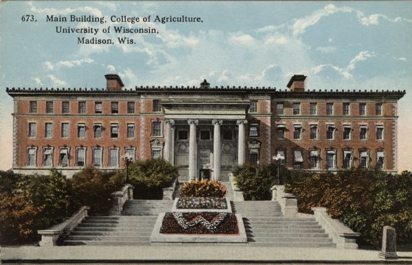 Facade of the main building of the College of Agriculture on the University of Wisconsin campus. A "W" flower bed is in front. Columns are at the entrance. Caption reads: Main Building, College of Agriculture, University of Wisconsin, Madison, Wis."