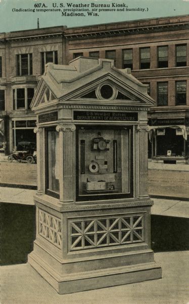 A weather kiosk located on Capitol Square, Department of Agriculture. It indicates temperature, precipitation, air pressure and humidity. A stationery shop and law offices are across the street. Caption reads: "U.S. Weather Bureau Kiosk, (indicating temperature, precipitation, air pressure and humidity.), Madison, Wis."