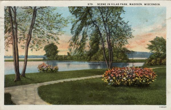 View of a walking path through Vilas Park along Lake Wingra, with flowering bushes and trees in the lawn. Caption reads: "Scene in Vilas Park, Madison, Wis."