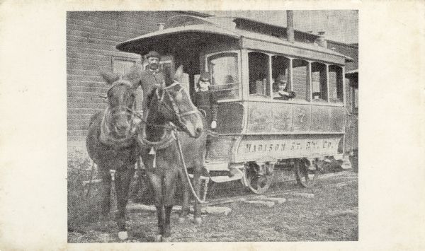 A streetcar pulled by two mules on a stretch of track. The driver and two children are on board. Text on reverse reads: "Madison Transportation. In 1885 Mr. Tom Shipway, who had been driving stage coach between Baraboo and Kilbourn, came to Madison and drove the mule cars from Jenifer and Brearly Sts. on the east side to University Ave. and Park St. on the west side. A third mule to help pull the car up King St. In the winter, straw on the floor and a coal stove to keep you warm. Madison Bus Co."