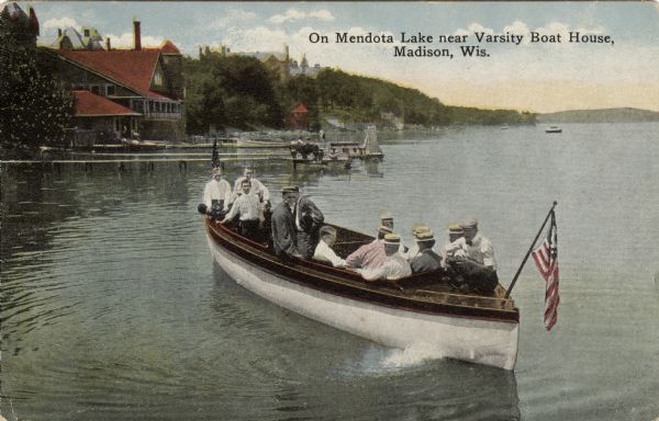 View across water towards people in an excursion boat on Lake Mendota heading towards a pier. The Varsity Boat House is in the background on the left shoreline. Caption reads: "On Mendota Lake near Varsity Boat House, Madison, Wis."