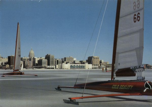 A winter's scene of ice boats on Lake Monona, with the Madison skyline featuring Monona Terrace and the Wisconsin State Capitol in the distance.
