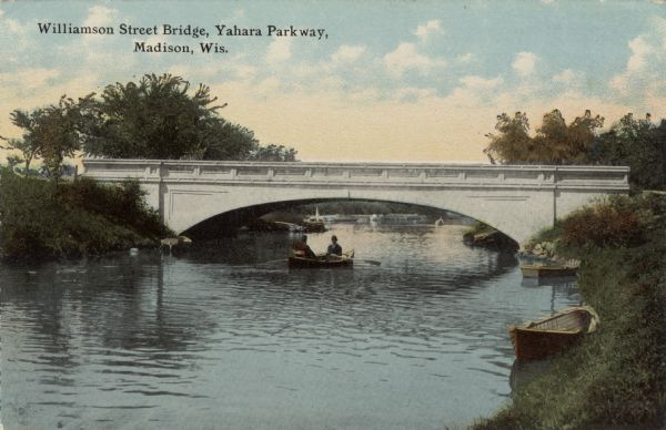 View of the Yahara River as it passes under the Williamson Street Bridge. Two people are in a rowboat near the bridge. Two boats are tied up near the shoreline on the right. Caption reads: "Williamson Street, Bridge, Yahara Parkway, Madison, Wis."