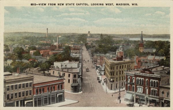 Elevated view of State Street from the Capitol. A streetcar is coming up the street, and automobiles are parked along the curbs. Lake Mendota is in the background on the right. The State Historical Society is at the end of State Street. Caption reads: "View from New State Capitol, Looking West, Madison, Wis."
