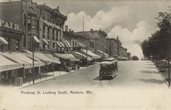 Slightly elevated view of Pinckney Street near Mifflin Street. A streetcar is coming down the street. There is a sign for the Academy of Music on a building on the left. The Capitol Square is on the right. Caption reads: "Pinckney St. Looking South, Madison, Wis."
