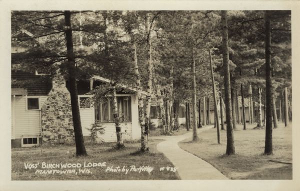 View down sidewalk towards cottages at a northwoods lodge. Caption reads: "Voss' Birchwood Lodge, Manitowish, Wis."