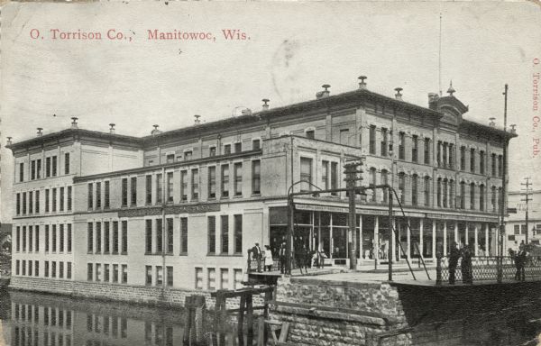View of the O. Torrison building on the north bank of the Manitowoc River. Caption reads: "O. Torrison Co., Manitowoc, Wis."