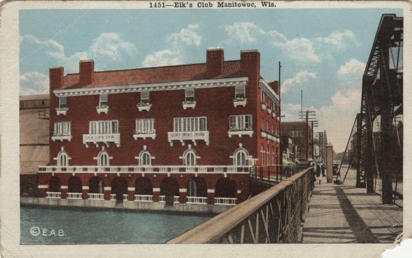 View from bridge towards the Elk's Club on the river's edge. Caption reads: "Elk's Club, Manitowoc, Wis."