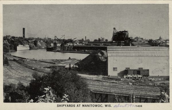 Photographic postcard view of the shipyards from across the river. Railroad tracks are in the foreground. Caption reads: "Shipyards at  Manitowoc, Wis."