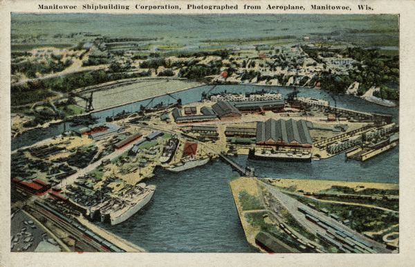 Aerial view of the shipyards built at the bend of the Manitowoc River. A railroad yard is in the foreground. Caption reads: "Manitowoc Shipbuilding Corporation, Photographed from Aeroplane, Manitowoc, Wis."